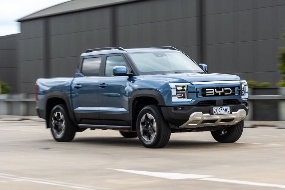 A blue 2026 BYD Shark 6 Premium dual-cab ute driving across a rooftop car park, seen from the front three-quarter angle