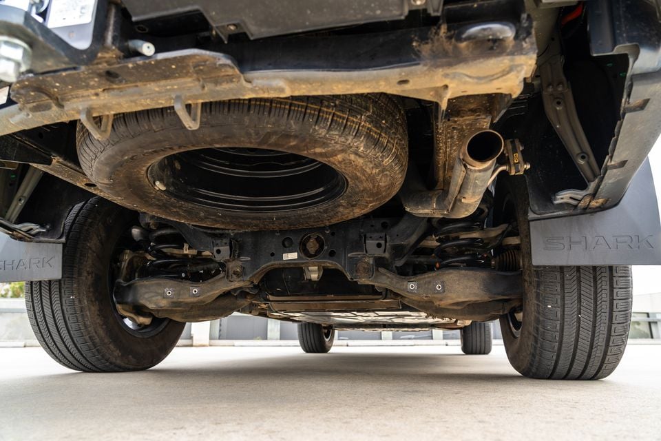 Underside of a 2026 BYD Shark 6 ute seen from behind, showing the underslung spare wheel, exhaust outlet, coil-spring rear suspension and Shark mud flaps