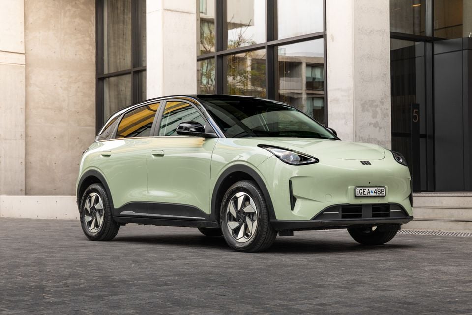 A light green 2026 Geely EX2 Inspire small SUV parked outside a modern building, seen from the front-left side