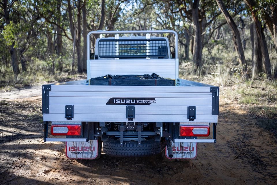 An Isuzu truck fitted with an aluminium tray body, seen from directly behind on a dirt track in the bush.
