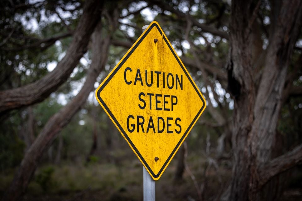 A yellow "Caution Steep Grades" road sign stands among trees on a bushland roadside.