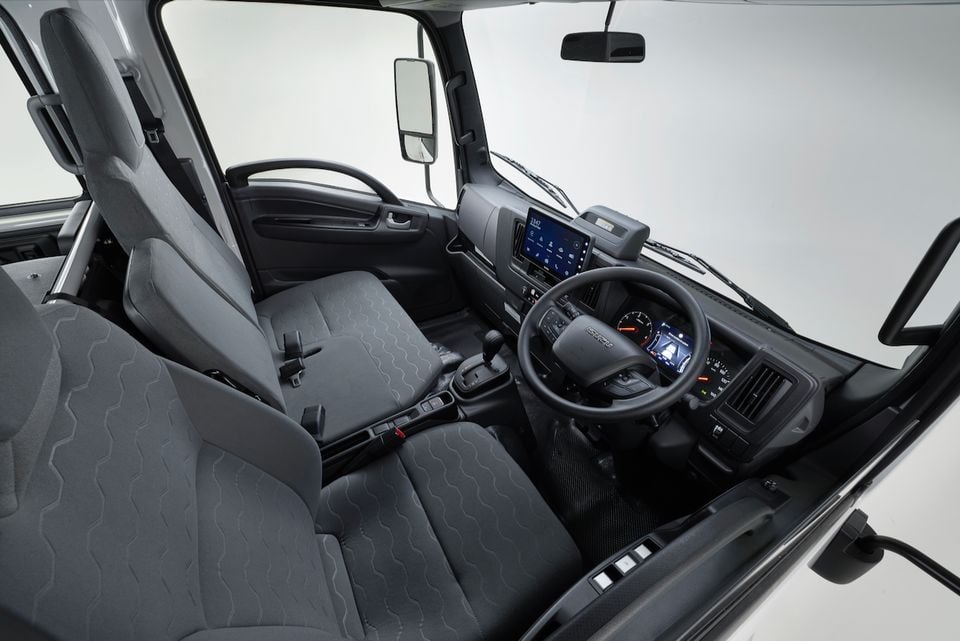 The cabin of a 2026 Isuzu NMS 45-150 AWD truck, showing the steering wheel, dashboard, infotainment screen and front seats.