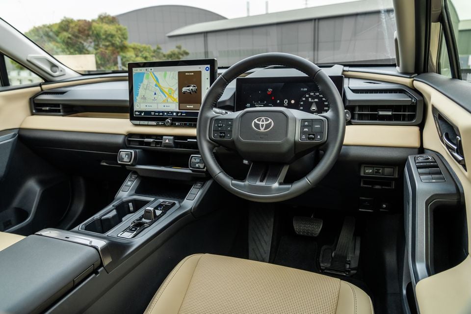 The interior of a 2026 Toyota RAV4 Cruiser shows the steering wheel, digital instrument cluster and touchscreen infotainment system in a beige and black cabin.