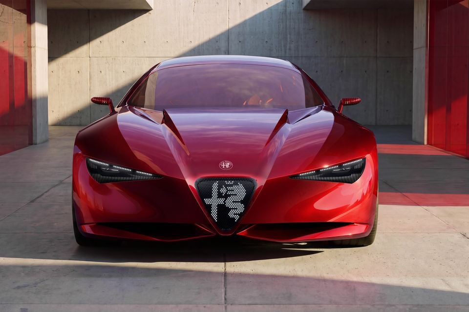 A red 2026 Alfa Romeo Cuorerosso concept car seen from the front, showing its illuminated triangular grille and slim headlights, parked in a concrete courtyard