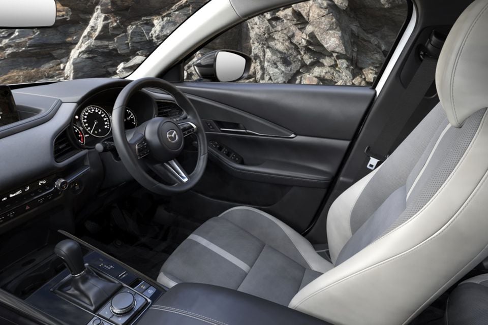 Interior of the 2026 Mazda CX-30 G25 GT SP showing the steering wheel, instrument cluster, gear selector and grey and white front seats