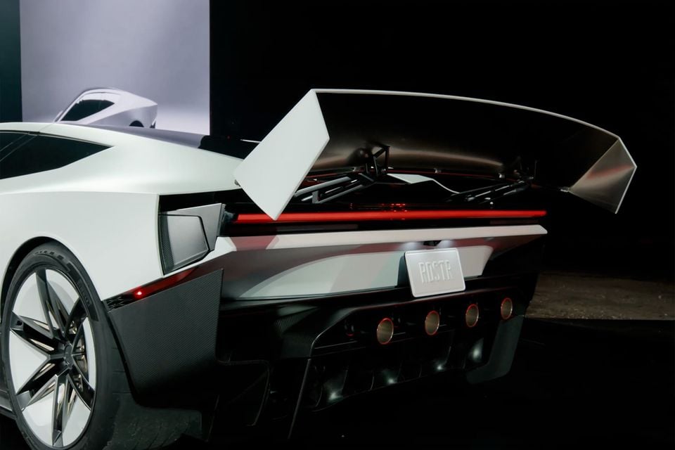 A white 2026 Tesla Roadster seen from the rear quarter, with its large active rear wing raised above a full-width red tail-light