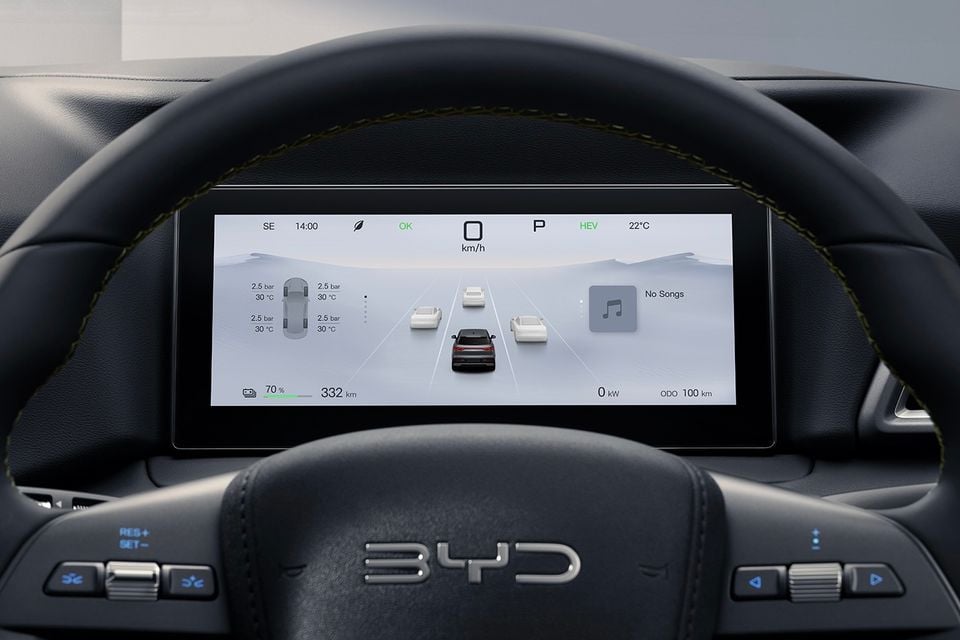 The digital instrument cluster of a BYD Atto 2 shows a driving assist display with vehicles ahead, speed, battery and range information, viewed through the steering wheel.