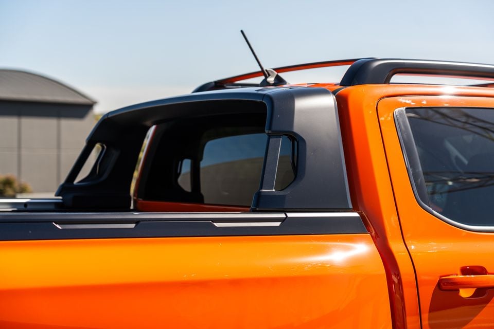 Close-up of the tray cover and rear cab area of an orange Ford Ranger Wildtrak ute, showing the sports bar and canopy detail against a clear sky.