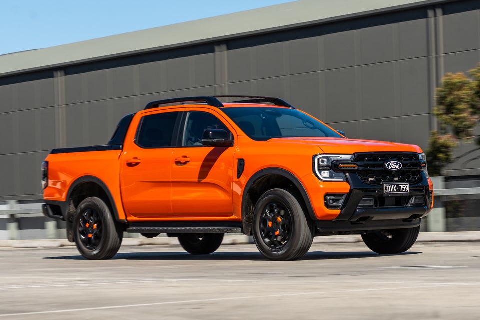 An orange Ford Ranger Wildtrak dual-cab ute seen from the front-side, driving past an industrial building
