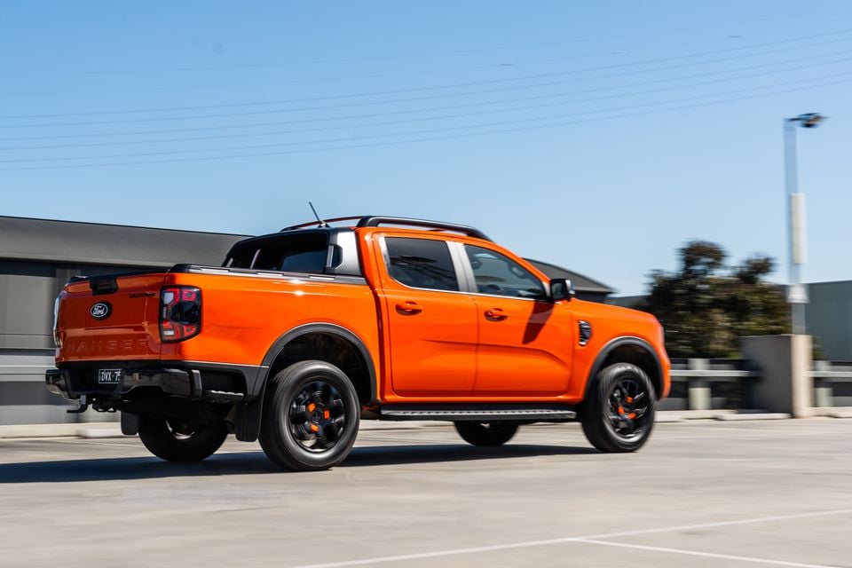 An orange Ford Ranger Wildtrak dual-cab ute seen from the rear three-quarter angle while driving through a car park