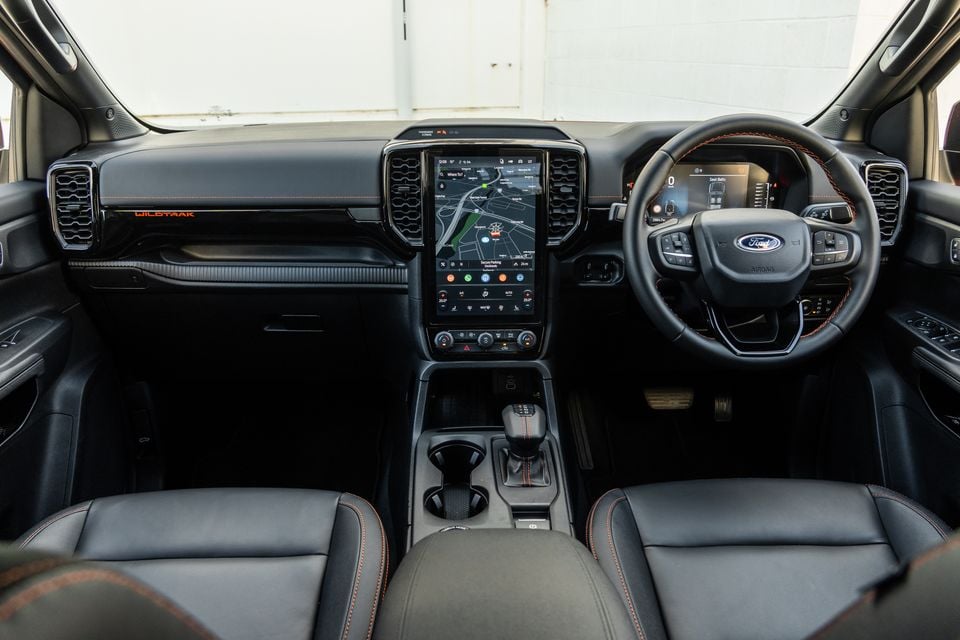 Interior of a Ford Ranger Wildtrak showing the large portrait touchscreen infotainment display, Ford steering wheel with orange stitching, centre console, and dashboard with Wildtrak badging on the dash trim