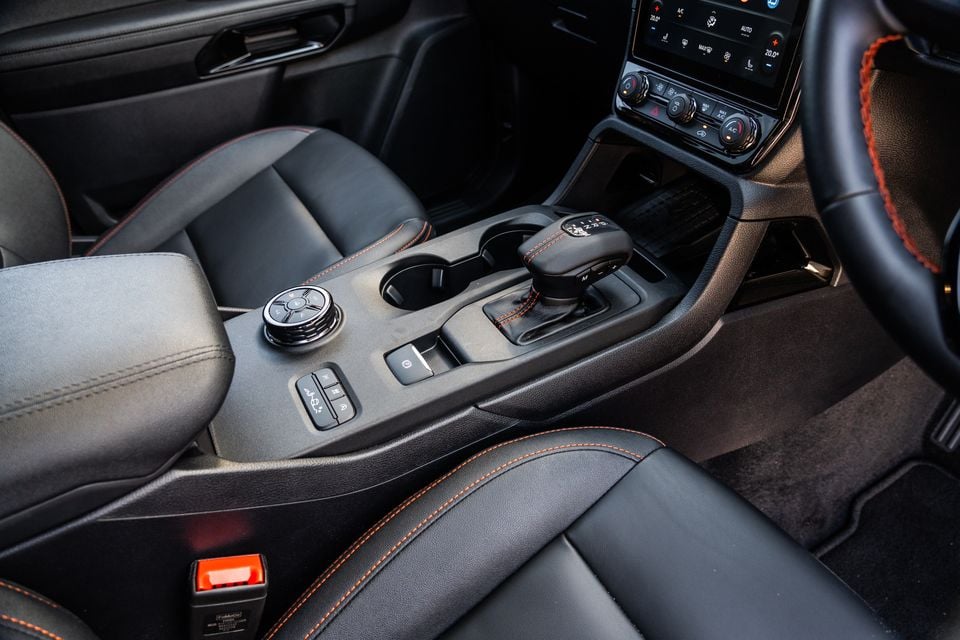 Interior centre console of the 2027 Ford Ranger Wildtrak showing the gear shifter, rotary dial, cup holders, and climate controls with orange contrast stitching on black leather seats