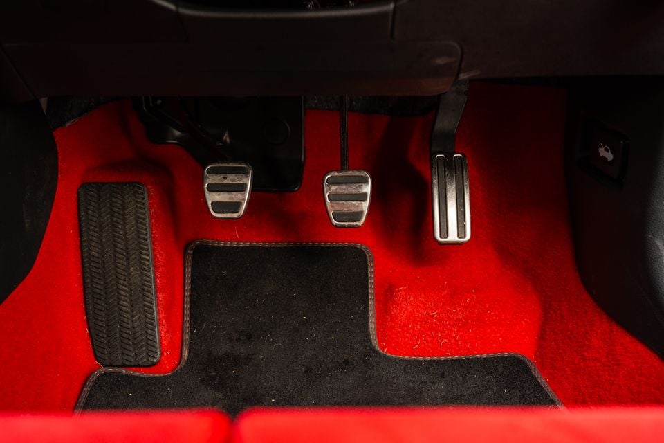 Close-up of the three aluminium sport pedals and red carpet floor of a Honda Civic Type R, showing the clutch, brake and accelerator pedals with a black floor mat