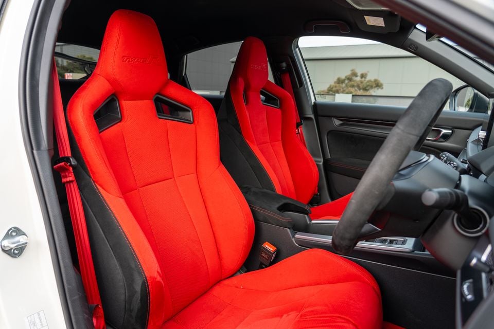 Red sport bucket seats with Type R branding inside a Honda Civic Type R, viewed from the passenger side door opening