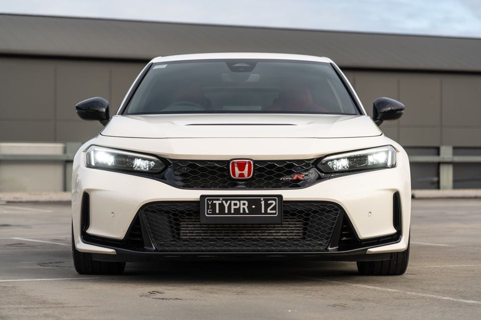 White Honda Civic Type R hatchback seen from the front in a car park, showing the aggressive grille, Honda badge and Type R badging
