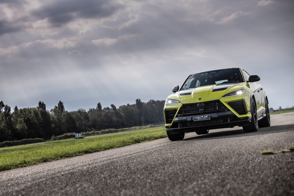 A lime green 2027 Lamborghini Urus SE Performante SUV driving on a race track under cloudy skies, seen from the front