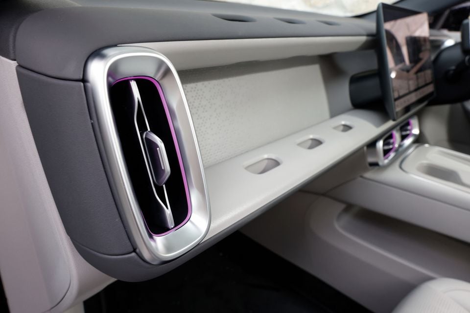 Passenger-side dashboard of the 2027 Leapmotor B05 with a chrome-ringed air vent, purple ambient lighting, a light grey shelf and a central touchscreen