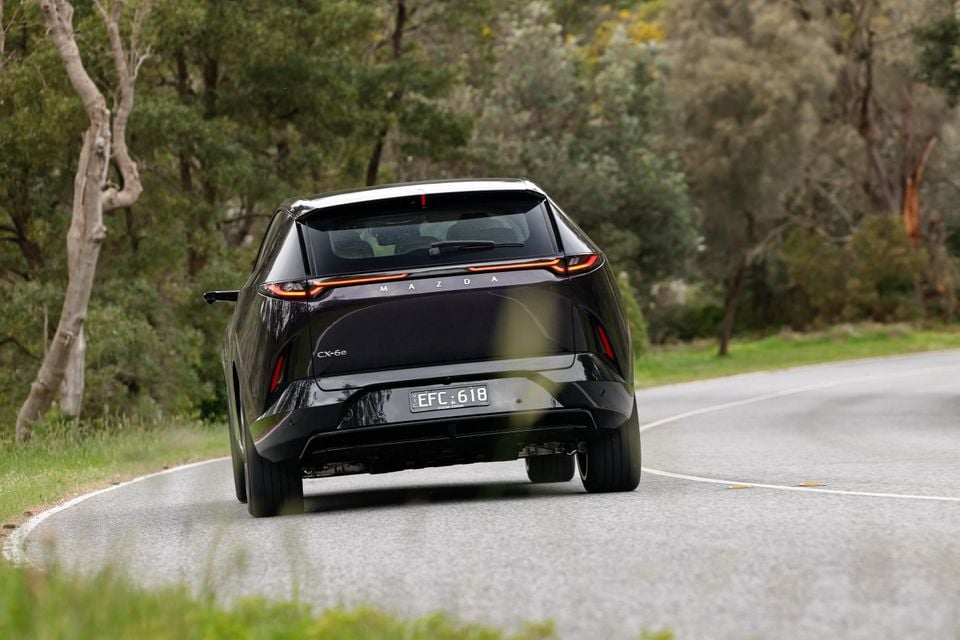 A black Mazda CX-6e SUV viewed from the rear while driving on a curved country road