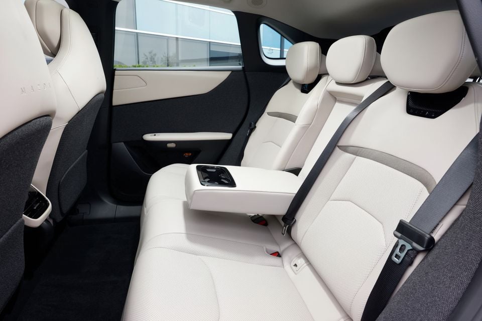 The rear seats and centre console of a 2027 Mazda CX-6e show cream leather upholstery and a folding armrest with cup holders.