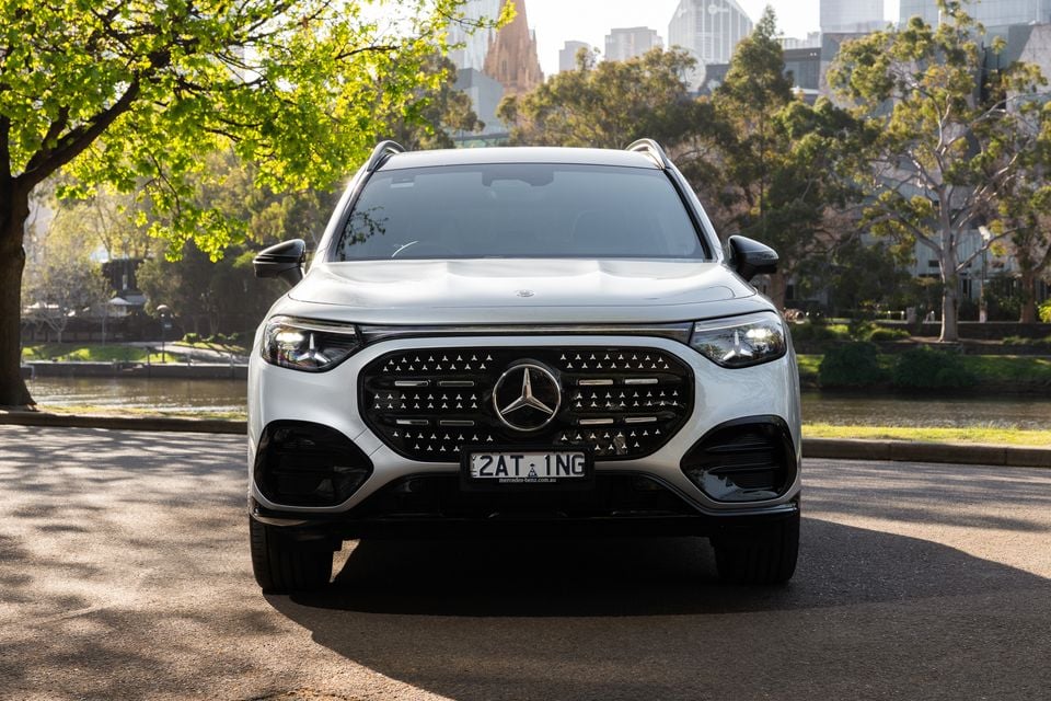 A white 2027 Mercedes-Benz GLB 350 4Matic electric SUV seen from the front, parked beside a river with city buildings behind