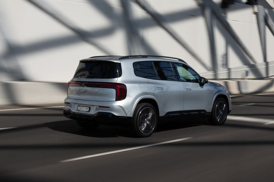 A silver 2027 Mercedes-Benz GLB 350 4Matic electric SUV driving across a bridge, seen from the rear quarter