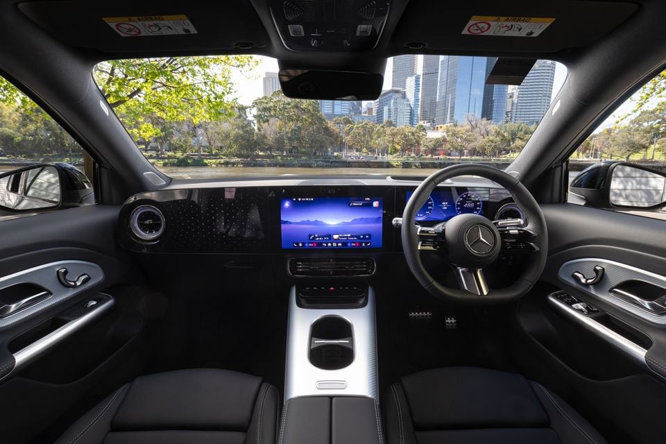 Dashboard of the 2027 Mercedes-Benz GLB 350 4Matic electric SUV with a central touchscreen, digital instrument cluster and steering wheel, overlooking a city river