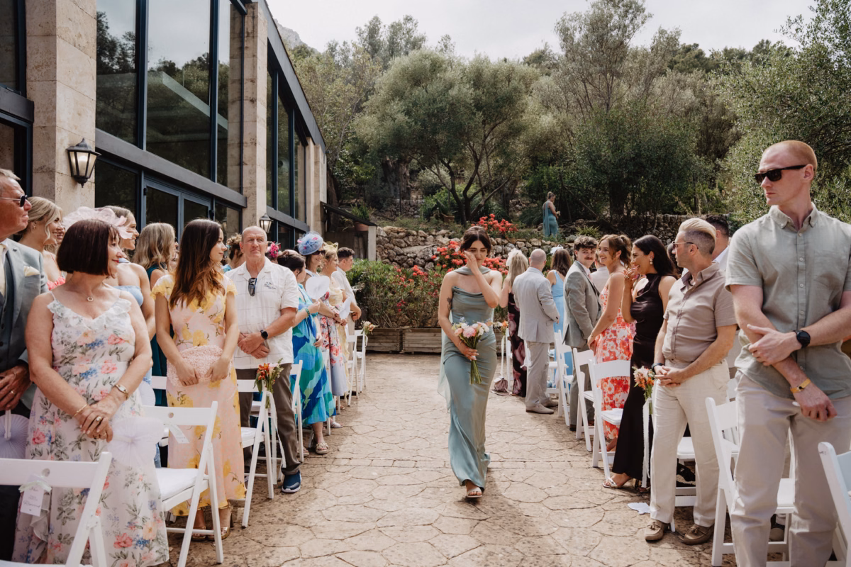 Mallorca Wedding Planner Dybiec Wedding Happiness Mode Photography 8 - How To Plan a Wedding in Mallorca From The UK, Part 2: Taking Your Wedding to Mallorca From the UK Emotional bridesmaid wiping a tear from her cheek as she walks down the outdoor aisle at a wedding in Mallorca, planned by Dybiec Wedding