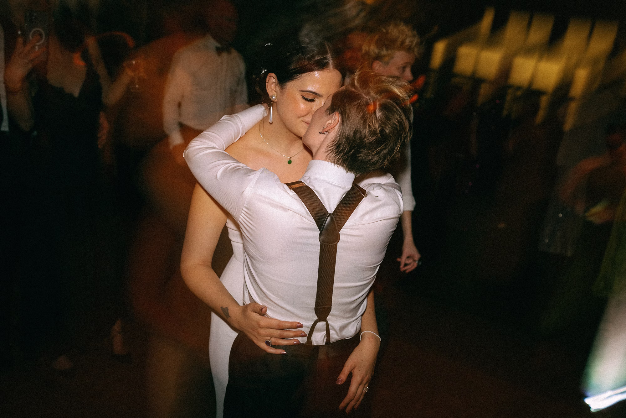 Newlyweds embracing on the dance floor, one wearing a strapless gown and the other a white shirt with braces