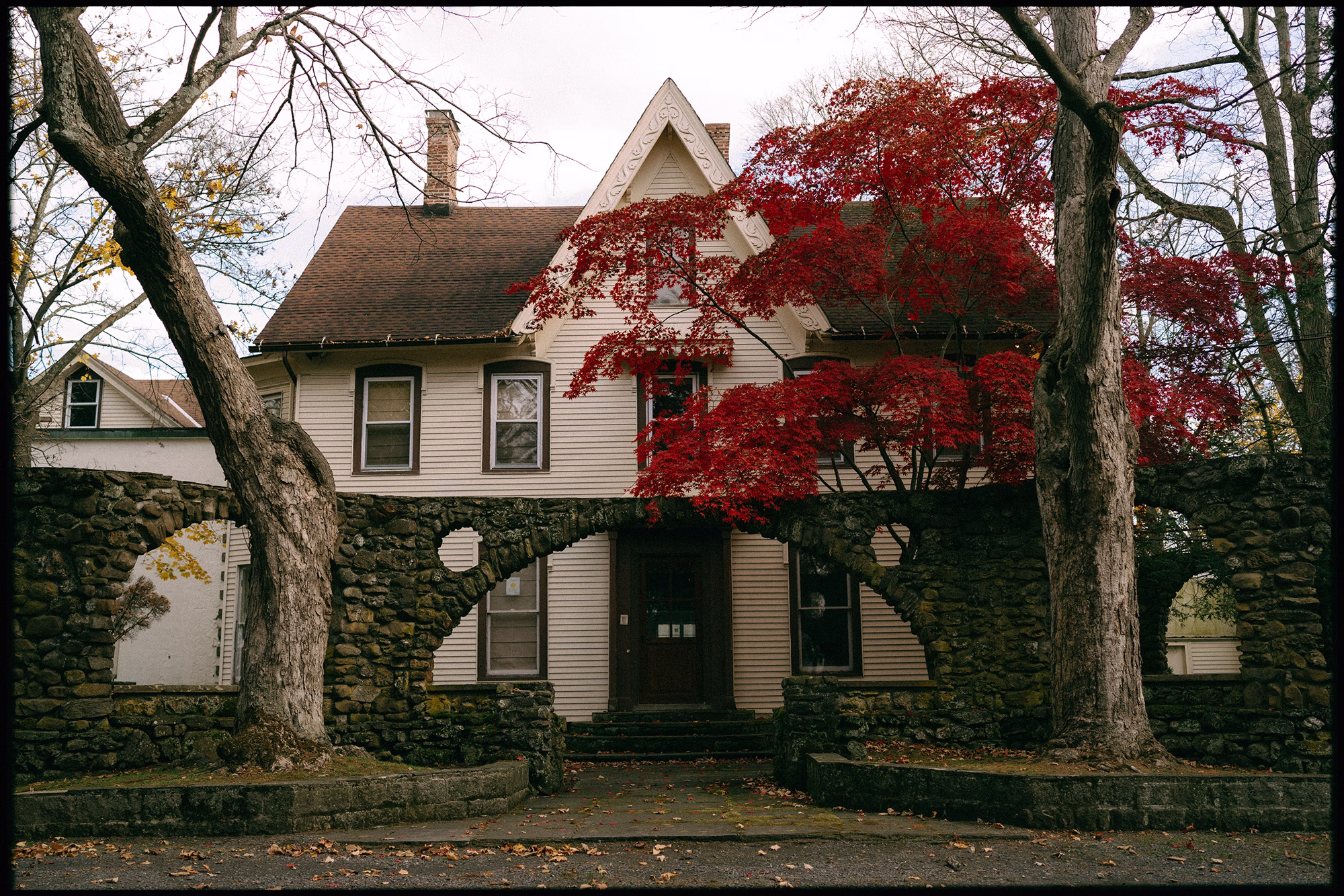 White gabled building behind stone arches and vivid red autumn foliage at Brotherhood Winery in New York