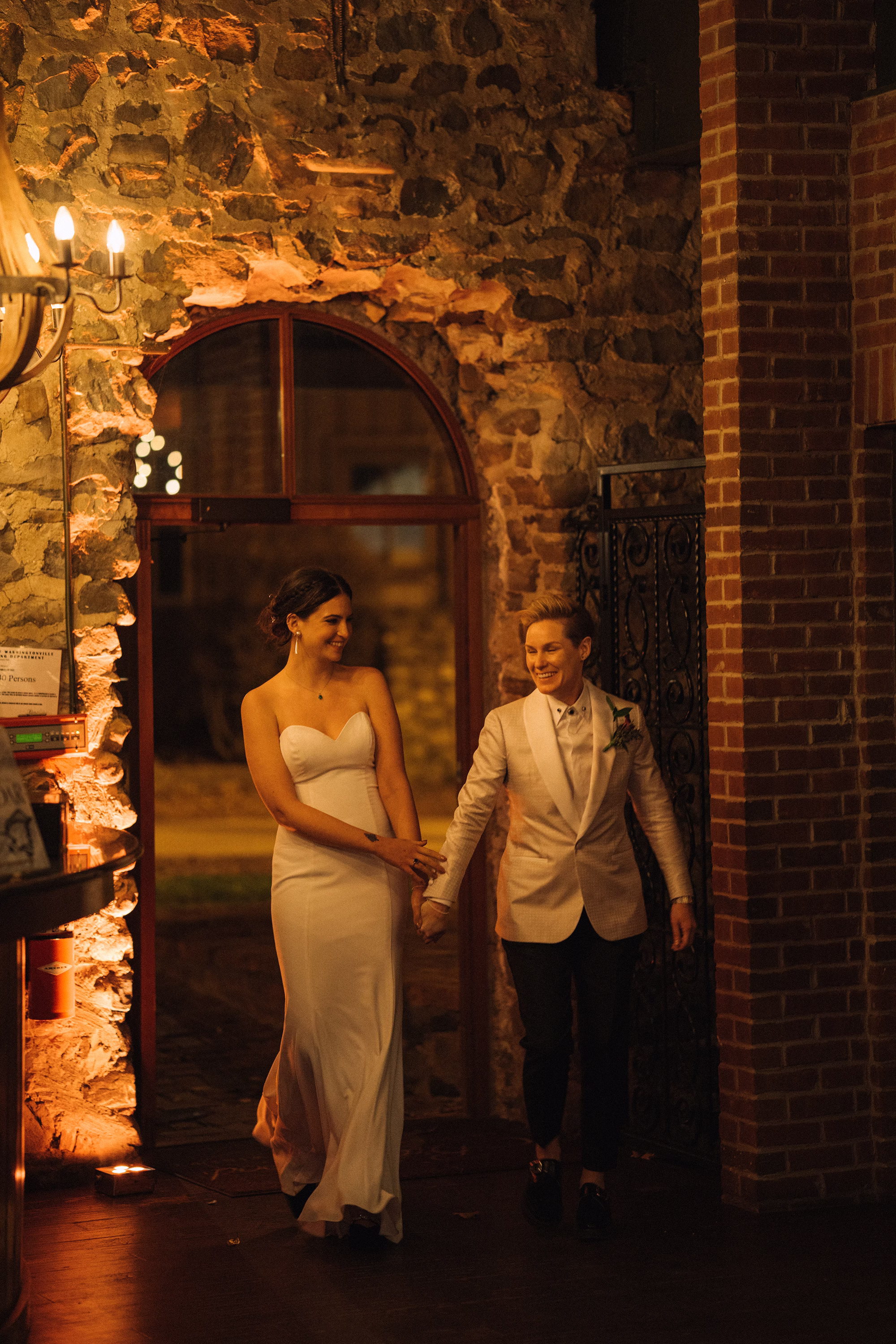 LGBTQ Newlyweds holding hands as they enter their wedding reception through an arched stone doorway