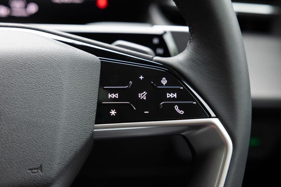 Close-up of the illuminated steering wheel controls on an Audi Q3, showing media, phone, voice and volume buttons on the left spoke