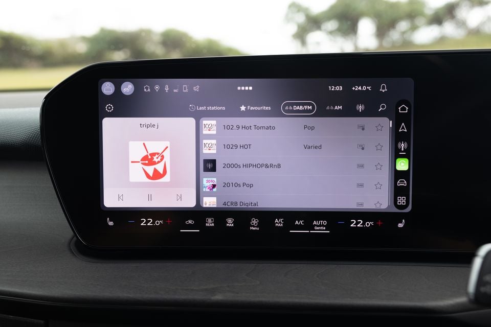 Volkswagen infotainment touchscreen displaying the DAB/FM radio menu with Triple J playing, showing a list of radio stations including 102.9 Hot Tomato, 1029 HOT, and 2000s Hip Hop and RnB, with climate controls visible below the screen