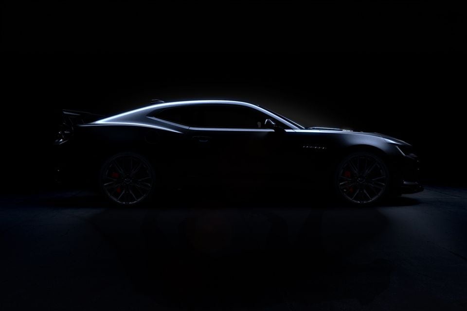 A Chevrolet Camaro coupe shown in dramatic silhouette against a dark studio background, viewed from the side