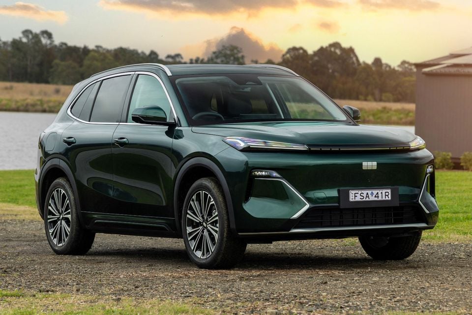 A dark green Geely Starray EM-i Inspire SUV seen from the front-side, parked on gravel near a lake at sunset