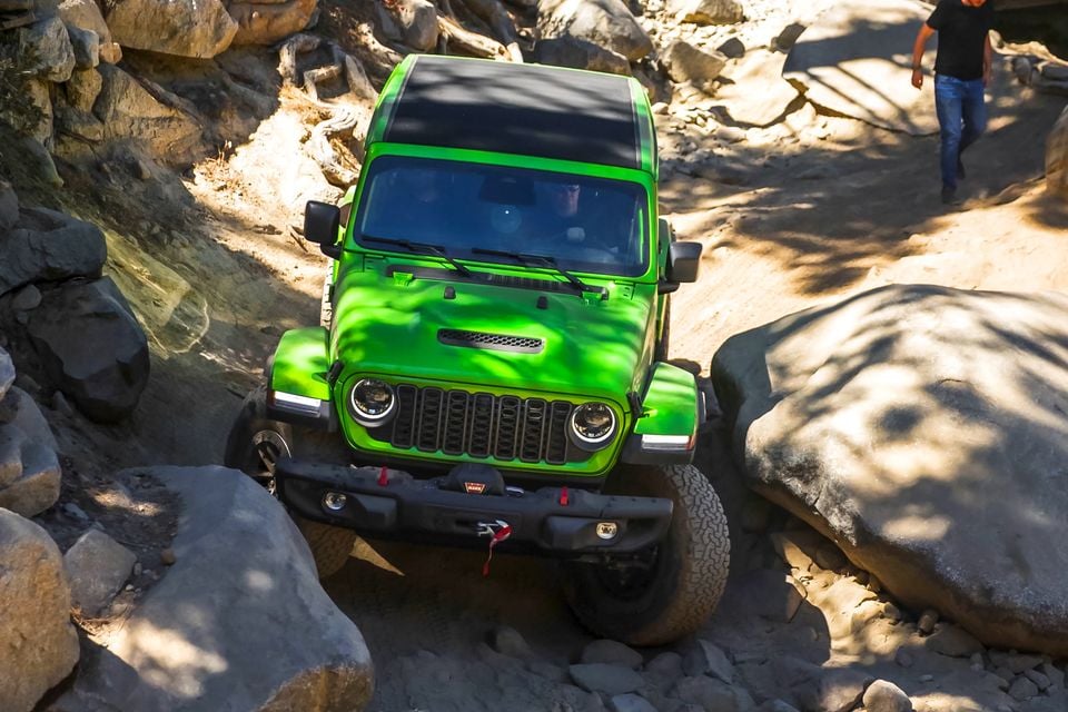 A green Jeep Wrangler 392 crawling over large boulders on the Rubicon Trail, seen from the front and slightly above