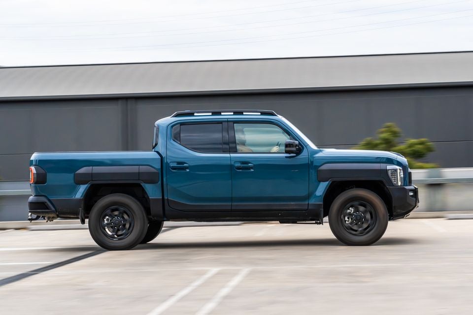A teal Kia Tasman X-Pro dual-cab ute seen from the side while driving along a road