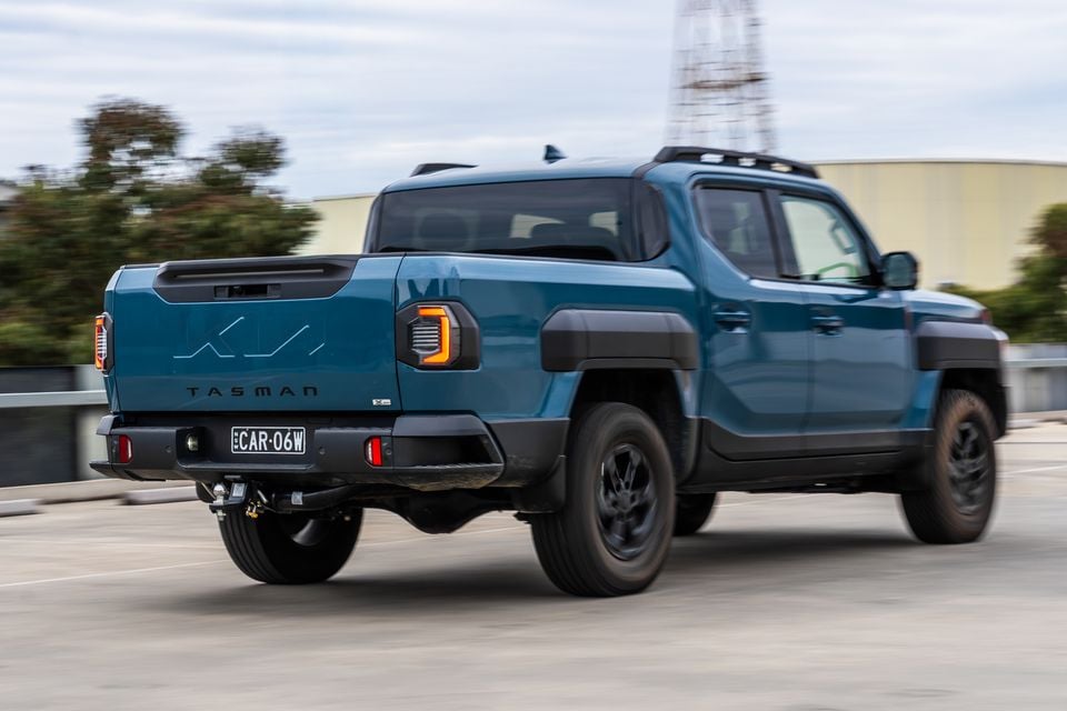 A teal Kia Tasman X-Pro dual-cab ute seen from the rear three-quarter angle while driving on a road