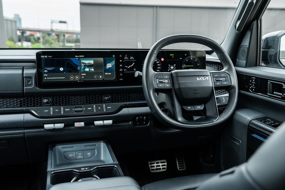 Kia Tasman interior showing the dashboard, wide infotainment touchscreen, digital instrument cluster, and steering wheel with Kia logo, in a right-hand drive layout