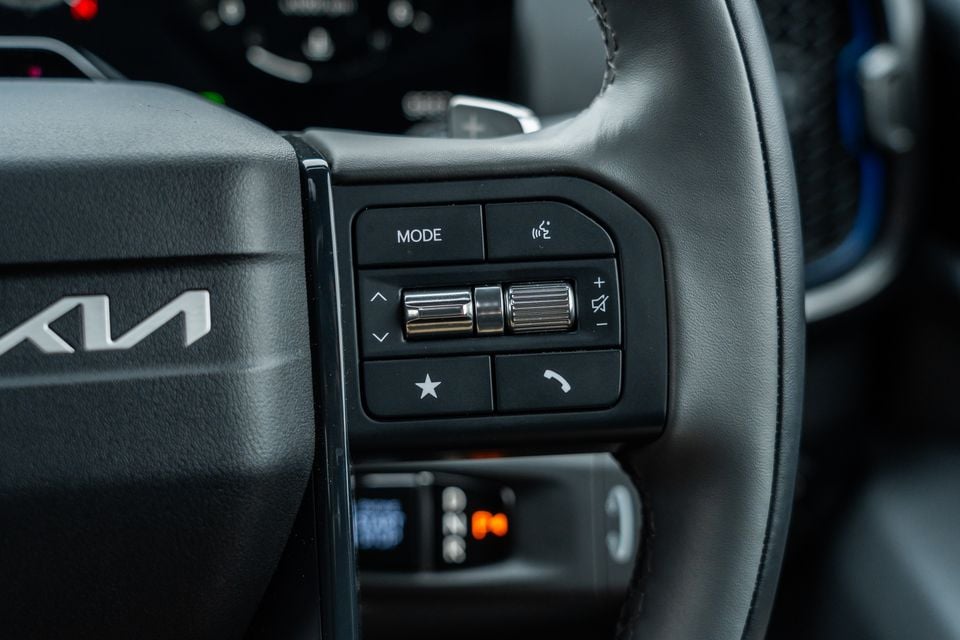 Close-up of the Kia Tasman steering wheel showing audio and phone control buttons including mode, volume, and voice controls