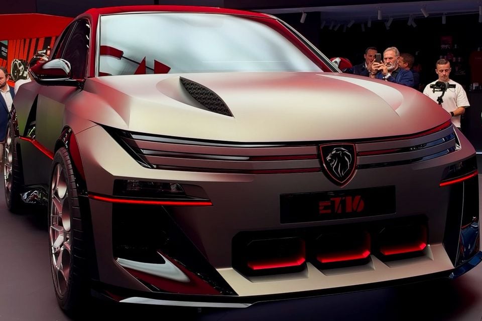 Peugeot E-T16 concept in matte silver with red accents, seen from the front at a motor show display as onlookers take photos