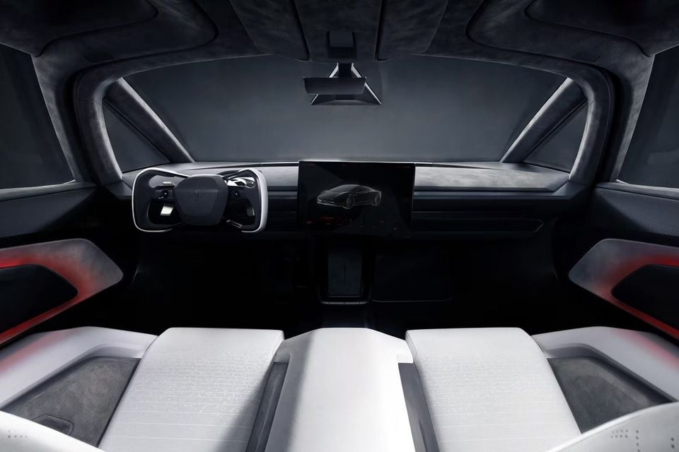 Dark cabin of an electric sports car with a white yoke-style steering wheel, large central touchscreen and white front seats